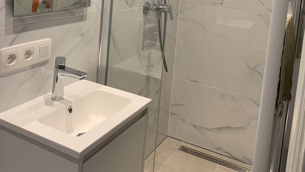 A modern bathroom with a glass-enclosed shower, a white sink, and a marble-tiled wall.