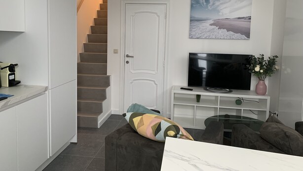 A modern living room with a flat-screen TV, a sofa, a coffee machine, and a staircase leading to another room. - Appartement Séparé Avec Parking Gratuit (Vilvoorde)
