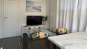 A modern living room with a flat-screen TV, a sofa with patterned cushions, a marble coffee table, and a painting of a beach scene on the wall. - Appartement Séparé Avec Parking Gratuit (Vilvoorde)