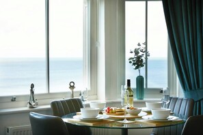 A dining table with white bowls, a wine bottle, and a glass of wine, set against a backdrop of a large window with a view of the sea. - This apartment is a 2 bedroom(s), 1 bathrooms, located in Scarborough, North Yorkshire. (Scarborough)