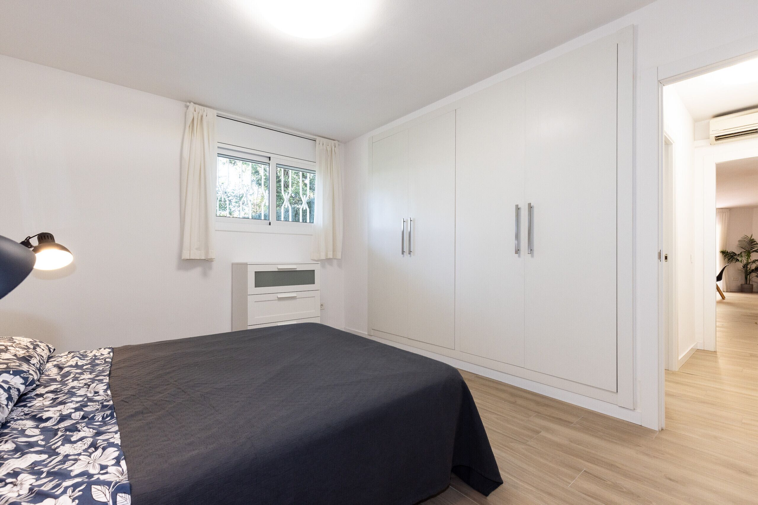 Ein Schlafzimmer mit Bett, Nachttisch, Kleiderschrank und einem Fenster mit Vorhängen.