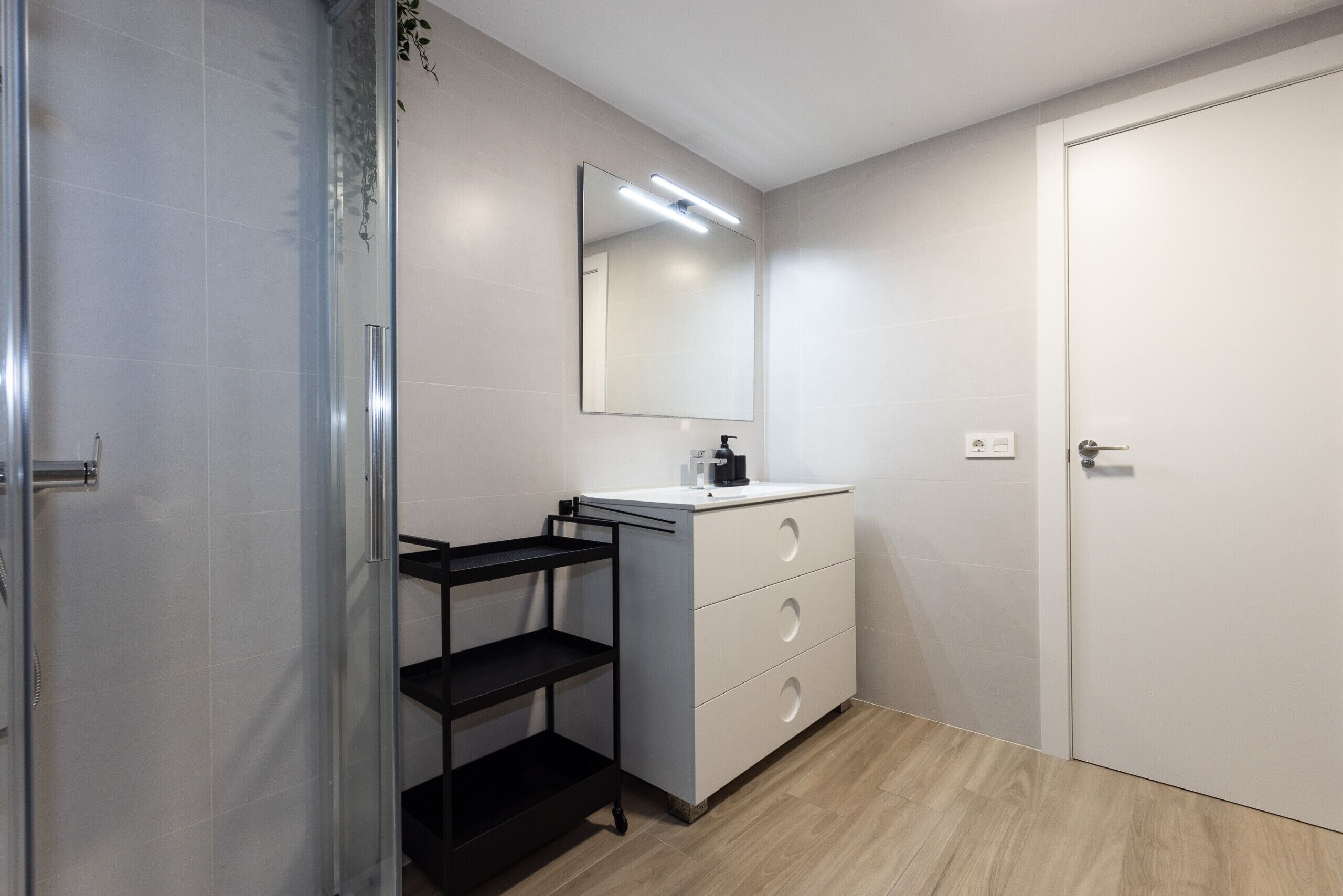 Un bagno moderno con box doccia in vetro, un mobile lavabo bianco con specchio e una scaffalatura nera.