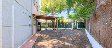 A covered outdoor area with a gravel path, trees, and a building wall.
