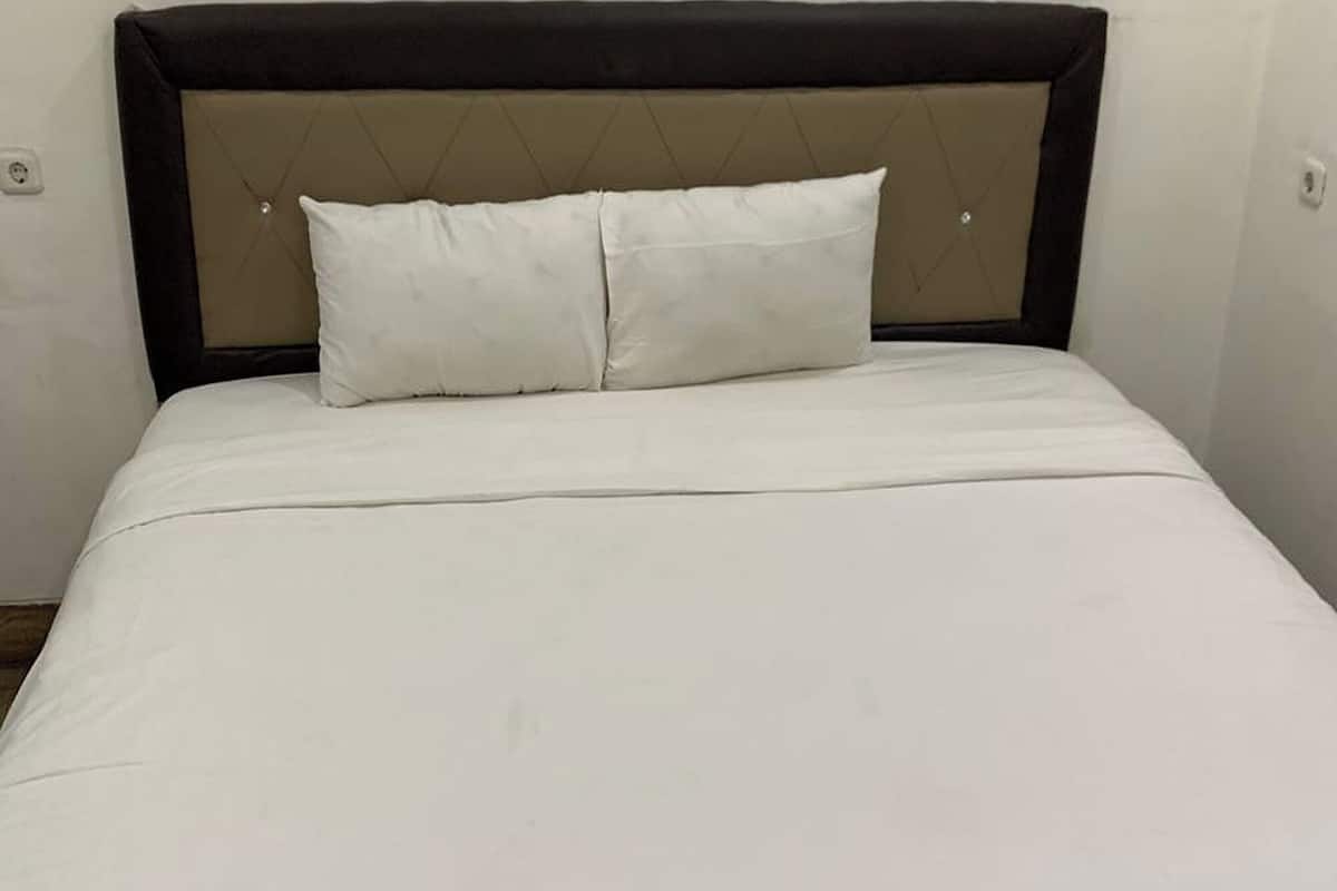 A bed with a headboard, two pillows, and a white bedspread.