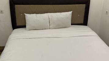 Een bed met hoofdbord, twee kussens en een witte spreideken.