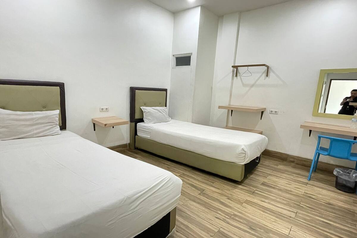 A hotel room with two single beds, a desk with a chair, a mirror, and a small window.