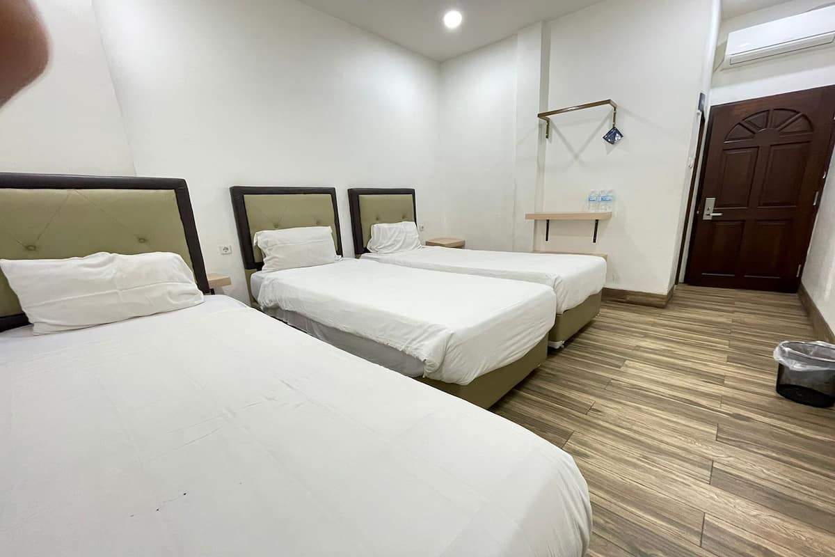 A hotel room with three beds, a small bedside table, a mirror, a shelf with toiletries, and a wooden floor.