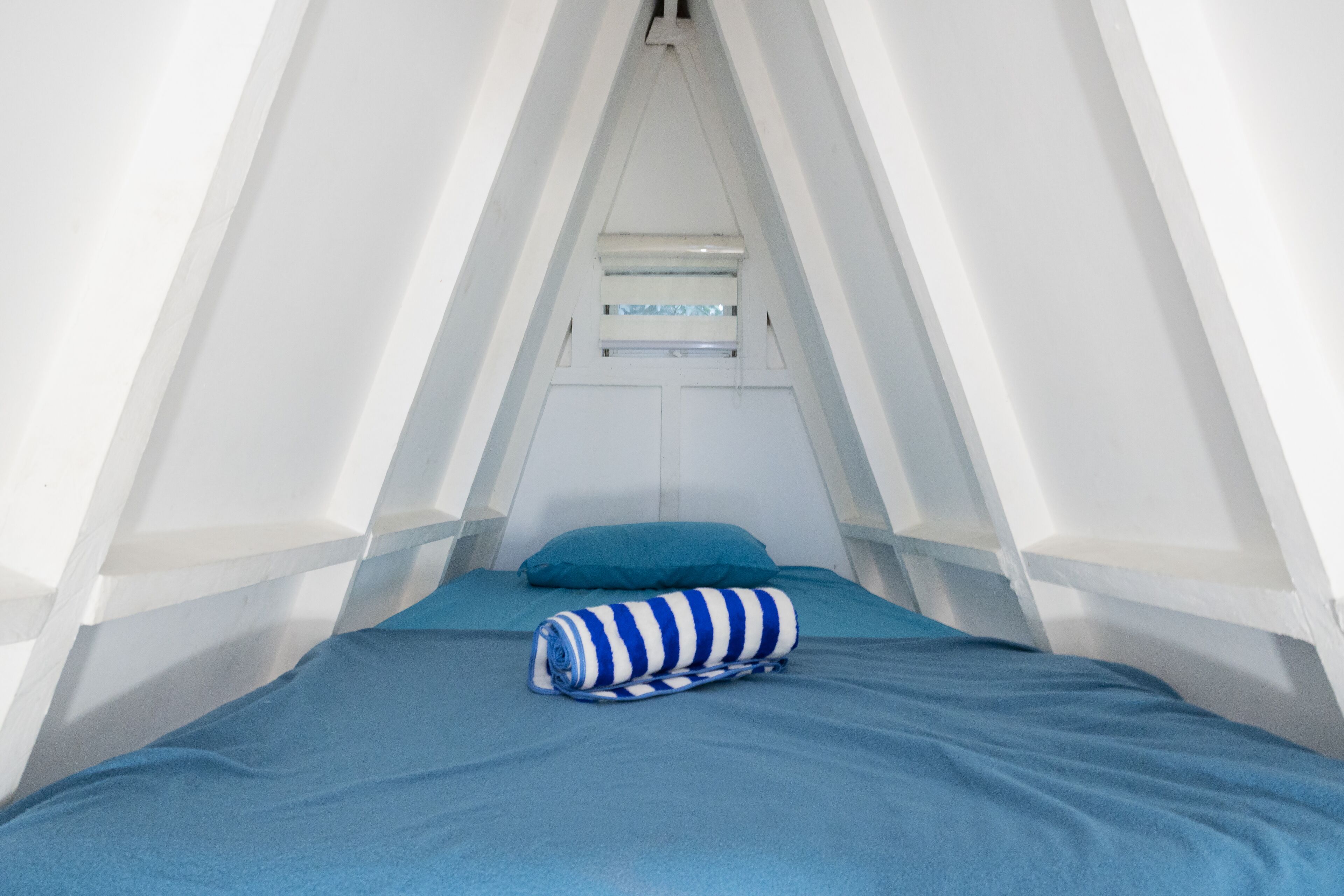 A triangular tent-like room with a bed, a pillow, and a striped blanket.