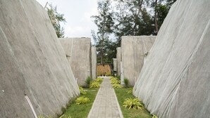 Ein Weg, der von Betonmauern gesäumt ist, mit einem kleinen Garten und einer Holzhütte im Hintergrund.