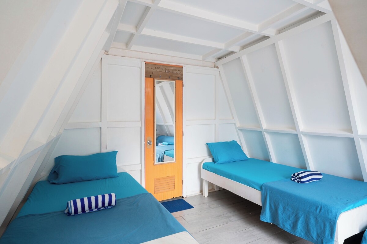 Une chambre avec deux lits, chacun recouvert d’une courtepointe bleue et agrémenté d’oreillers, et une porte en bois avec un miroir.