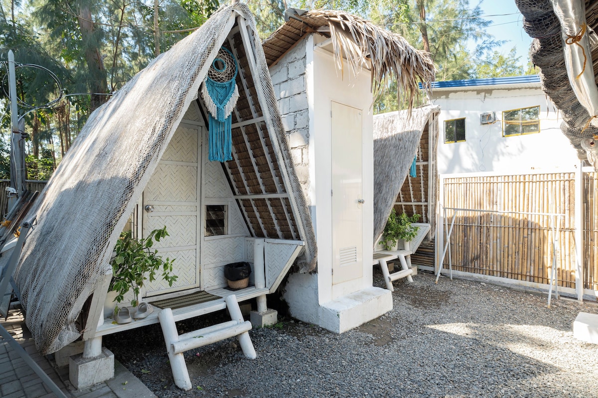 Een klein, rustiek vakantiehuisje met rieten dak, een bankje en een tafeltje met een plant.