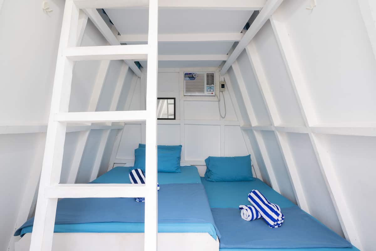 Una habitación con dos camas, cada una con ropa de cama y almohadas azules, y una escalera blanca.