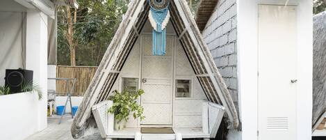 A small, white, triangular-shaped structure with a door and a bench.