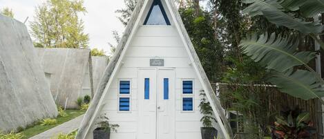 A white triangular building with a peaked roof, two doors with blue windows, and a sign above the doors.