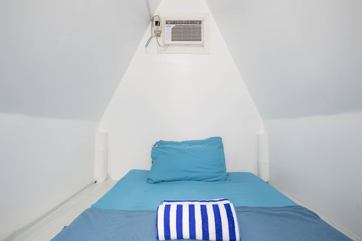 Una habitación pequeña con una cama individual, techo inclinado y aire acondicionado integrado.