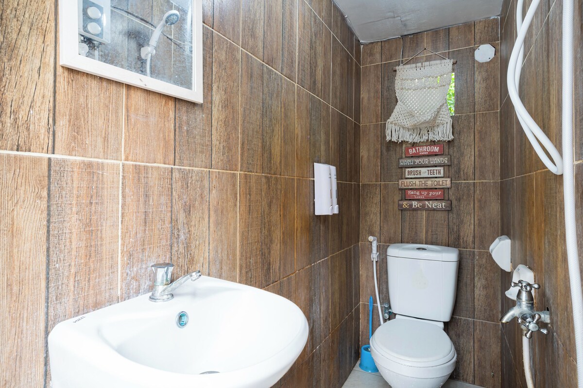 Une salle de bain avec des murs en bois, un lavabo blanc, des toilettes et une douche. Un panneau indiquant les consignes d’utilisation de la salle de bain est accroché au mur.