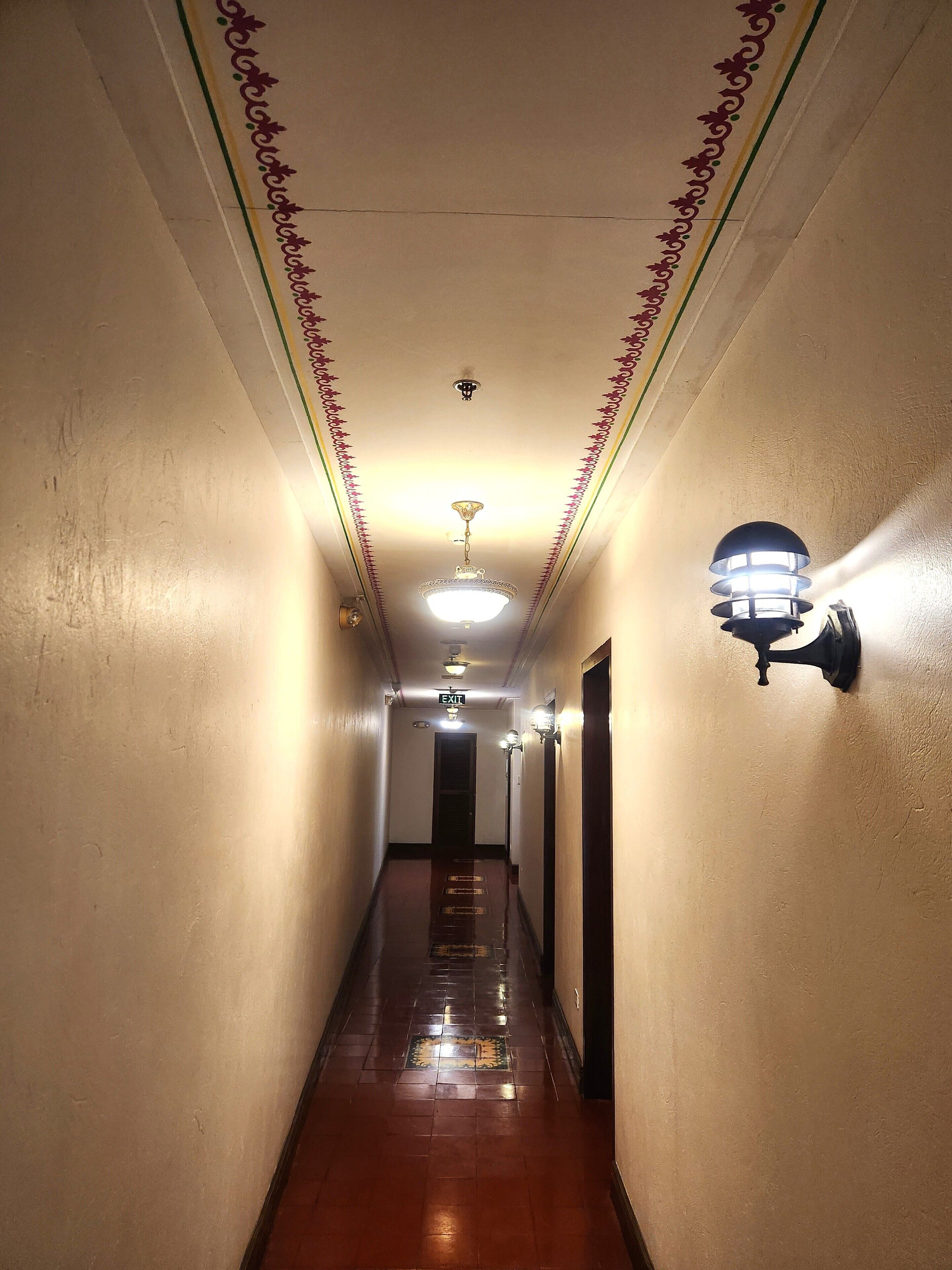 A narrow, well-lit hallway with patterned walls and a tiled floor, leading to an exit door.