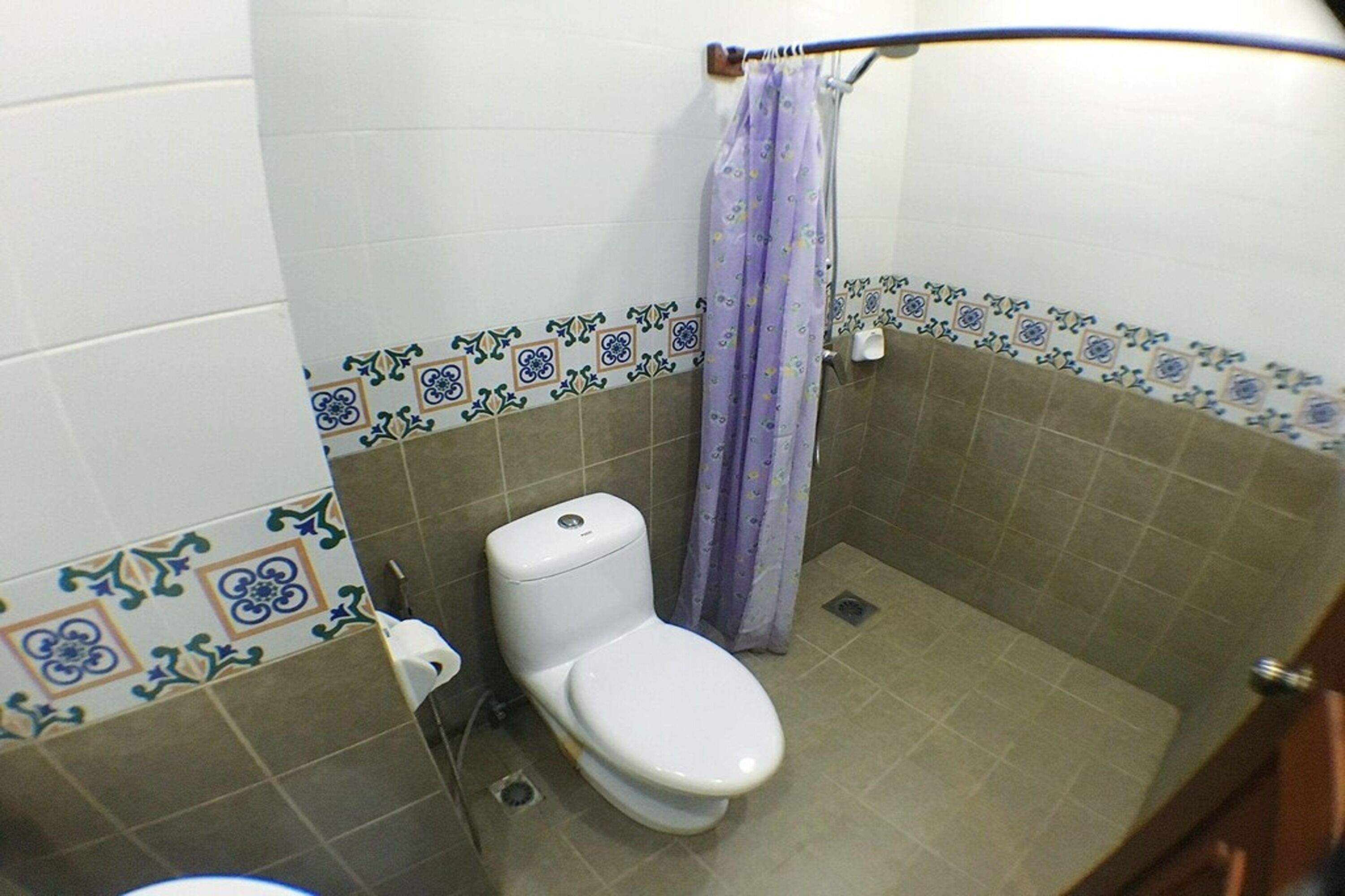 Un baño con inodoro, cortina de ducha y azulejos decorativos.