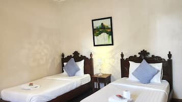 Een hotelkamer met twee eenpersoonsbedden, houten hoofdborden, witte linnens en een schilderij aan de muur, plus een klein nachtkastje met een lamp.