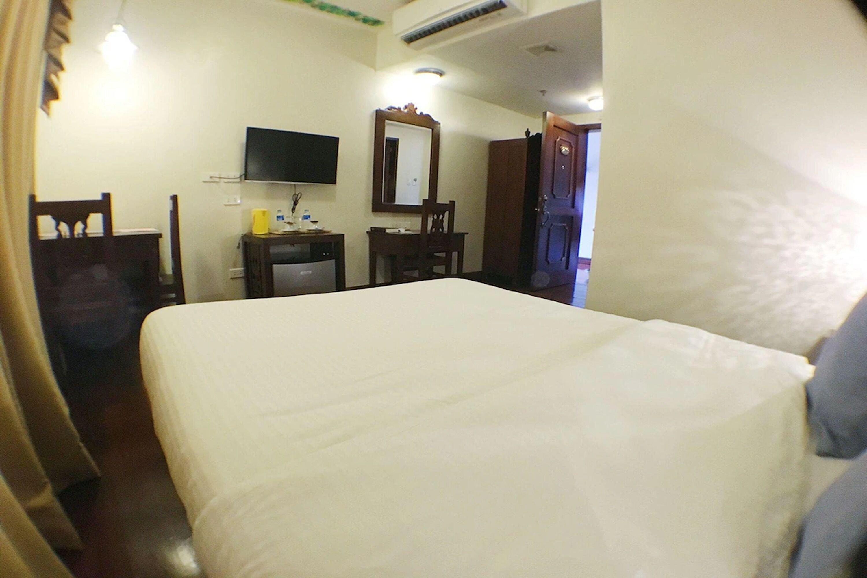 A hotel room with a bed, a desk, a chair, a television, and a door.