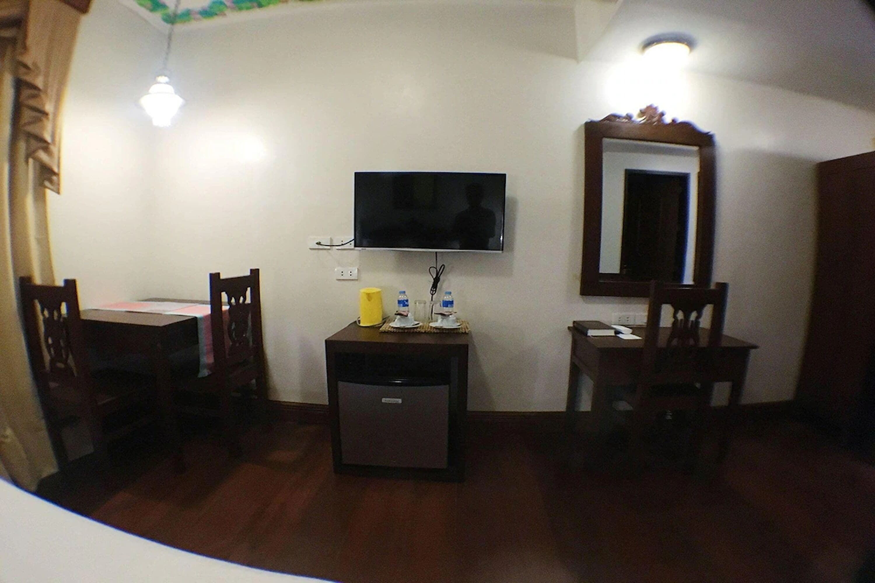 Una habitación pequeña con una televisión montada en la pared, un escritorio con una silla y un mueble auxiliar.