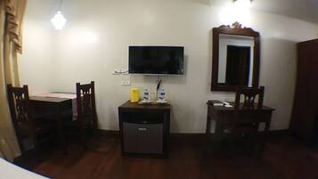 Una habitación pequeña con una televisión montada en la pared, un escritorio con una silla y un mueble auxiliar.