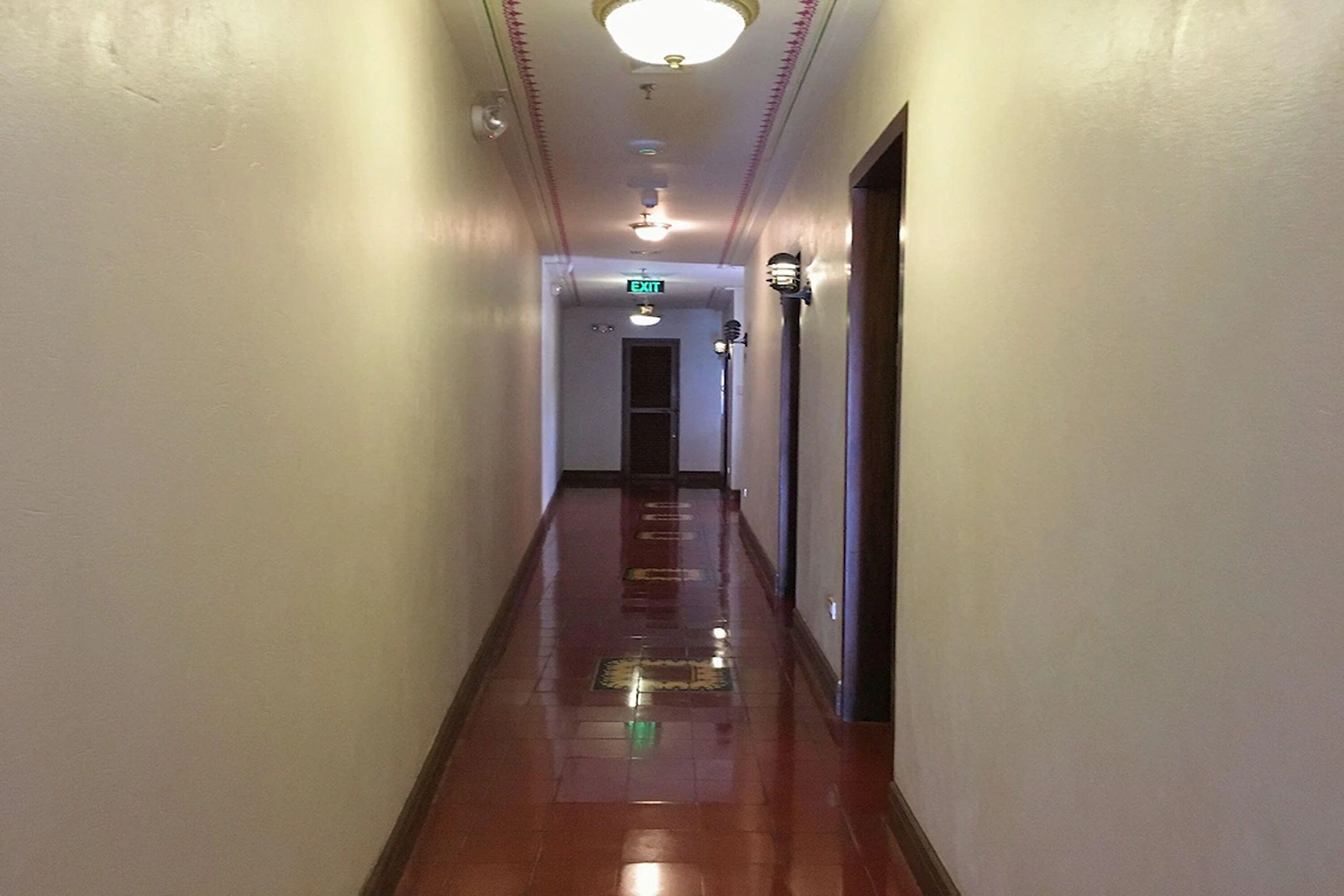 A hallway with a shiny floor, white walls, and an exit sign.