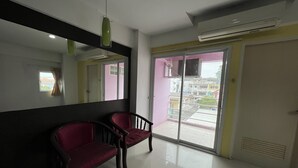 A hotel room with a large mirror, two red chairs, a sliding glass door, and an air conditioning unit. - Phongsathon Mansion (Bangkok)