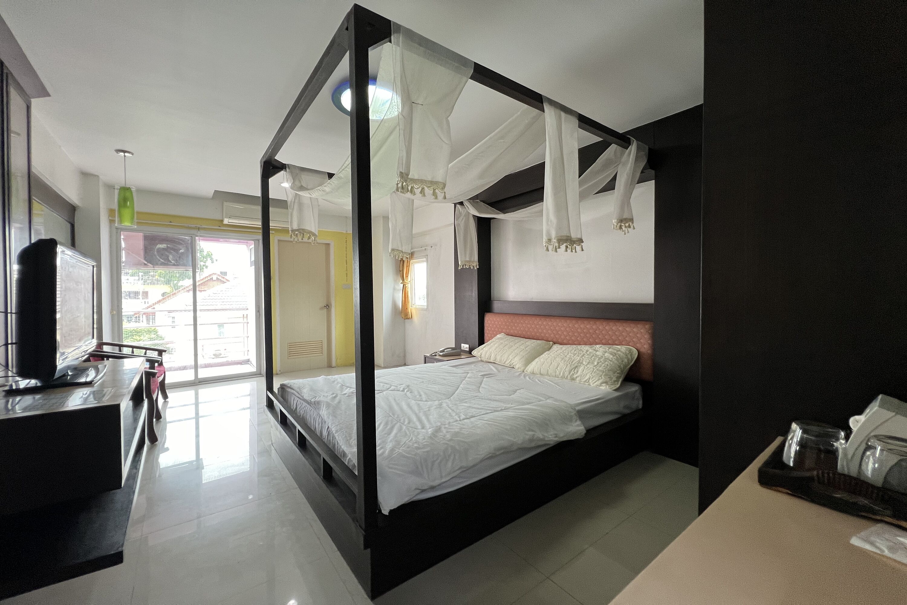 A modern hotel room with a large bed, a desk with a computer, and a view of the outside.