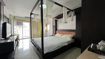 A modern hotel room with a large bed, a desk with a computer, and a view of the outside.