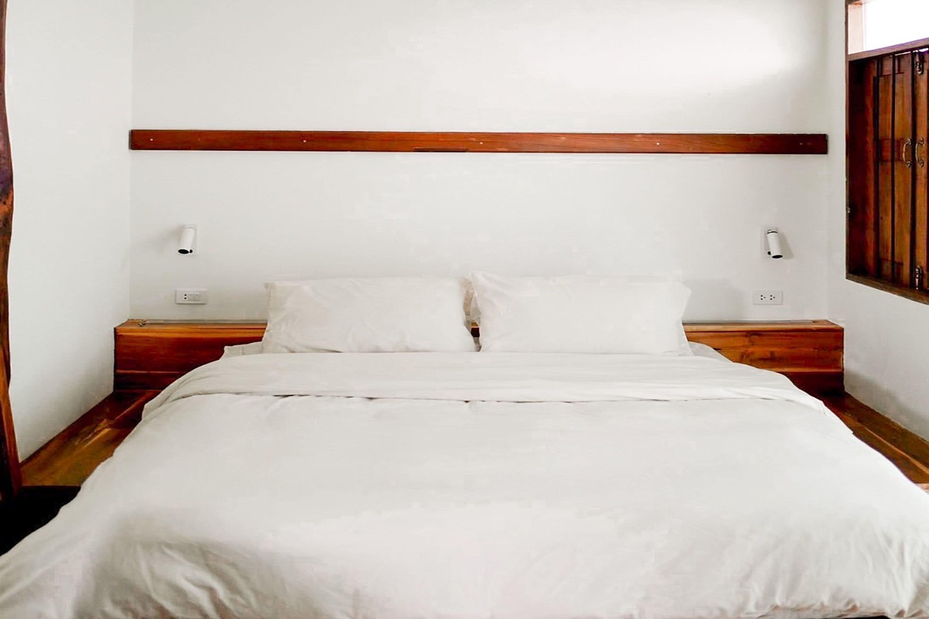 A neatly made bed with white linens, wooden headboard, and nightstands with lamps.