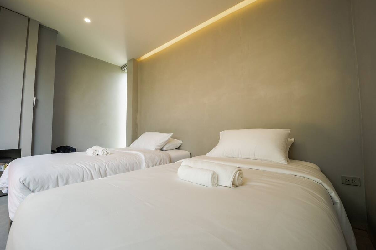 A hotel room with two beds, each with white linens and pillows, and a neutral-colored wall.