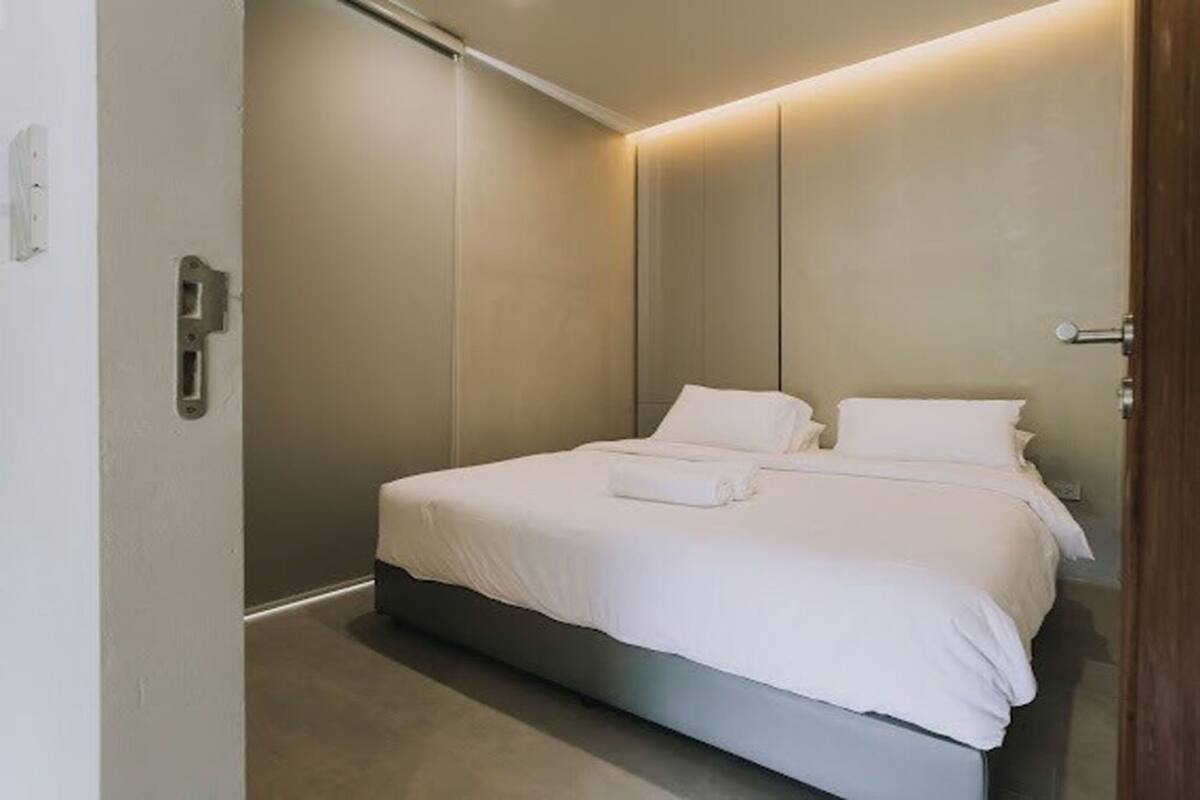 A modern bedroom with a large bed, a bedside table, and a wall-mounted light fixture.