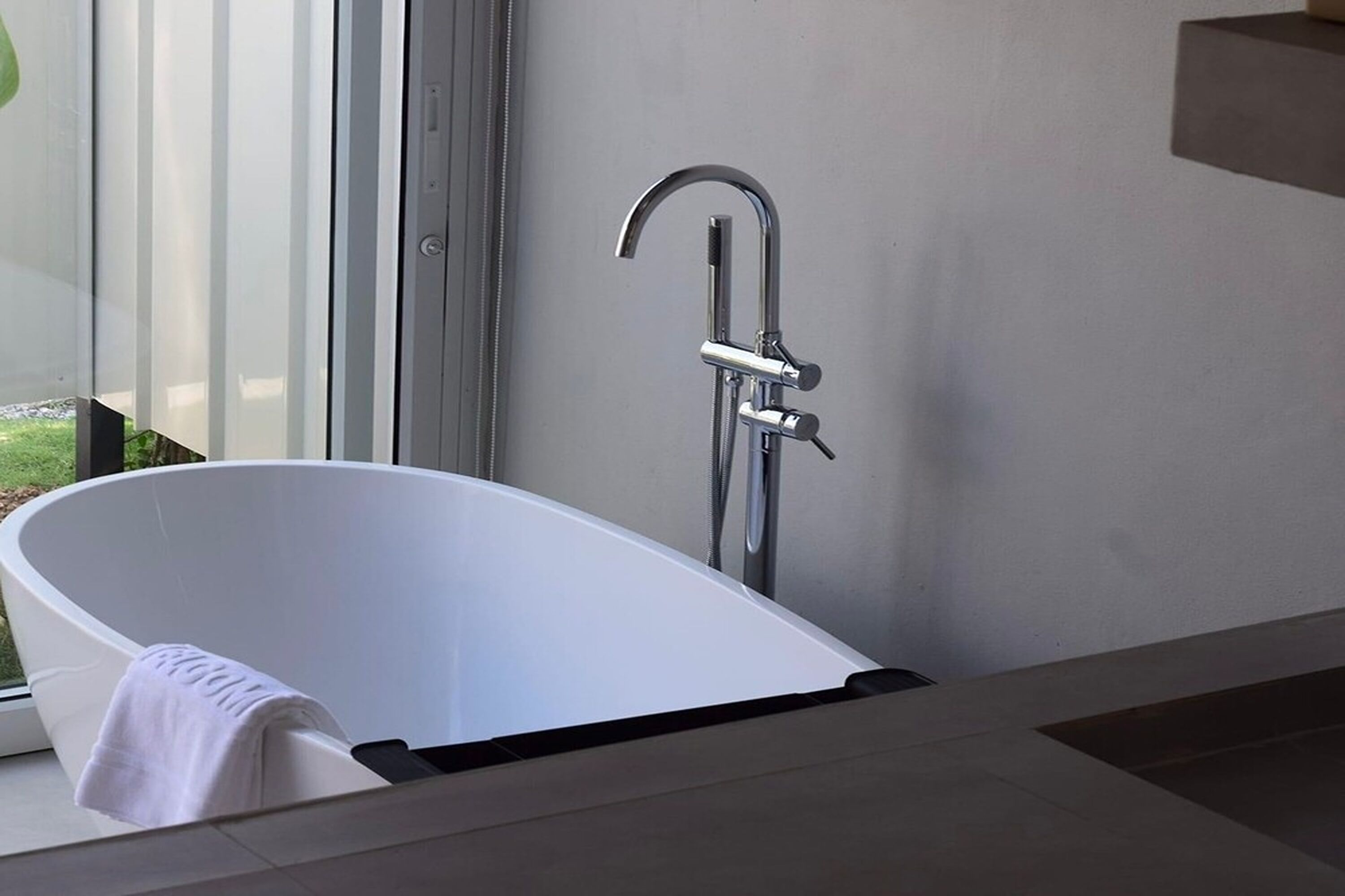 Een moderne badkamer met een vrijstaand bad, een chromen kraan en een raam met uitzicht op de natuur.