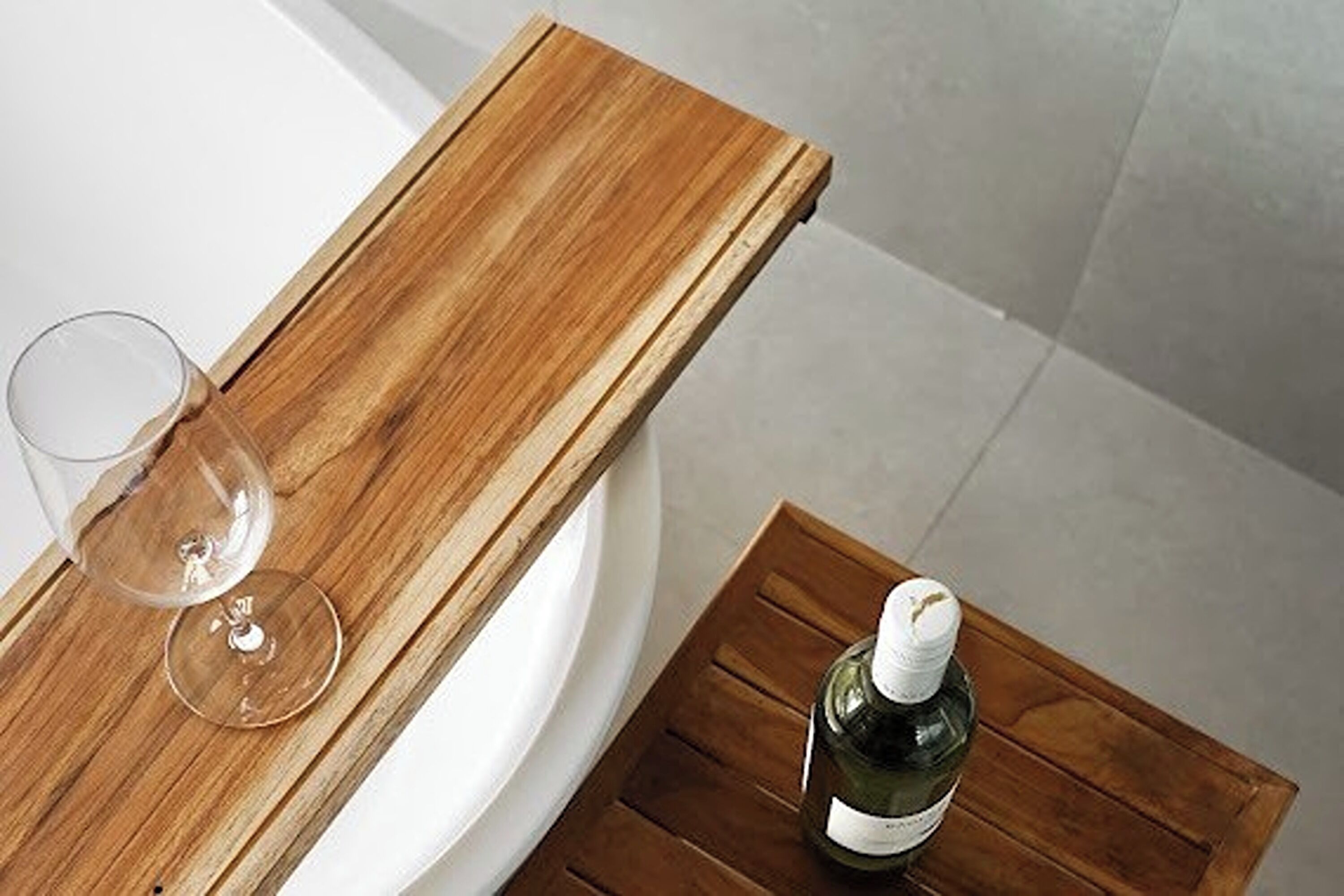 A wooden table with a wine glass and bottle, positioned near a white bathtub.