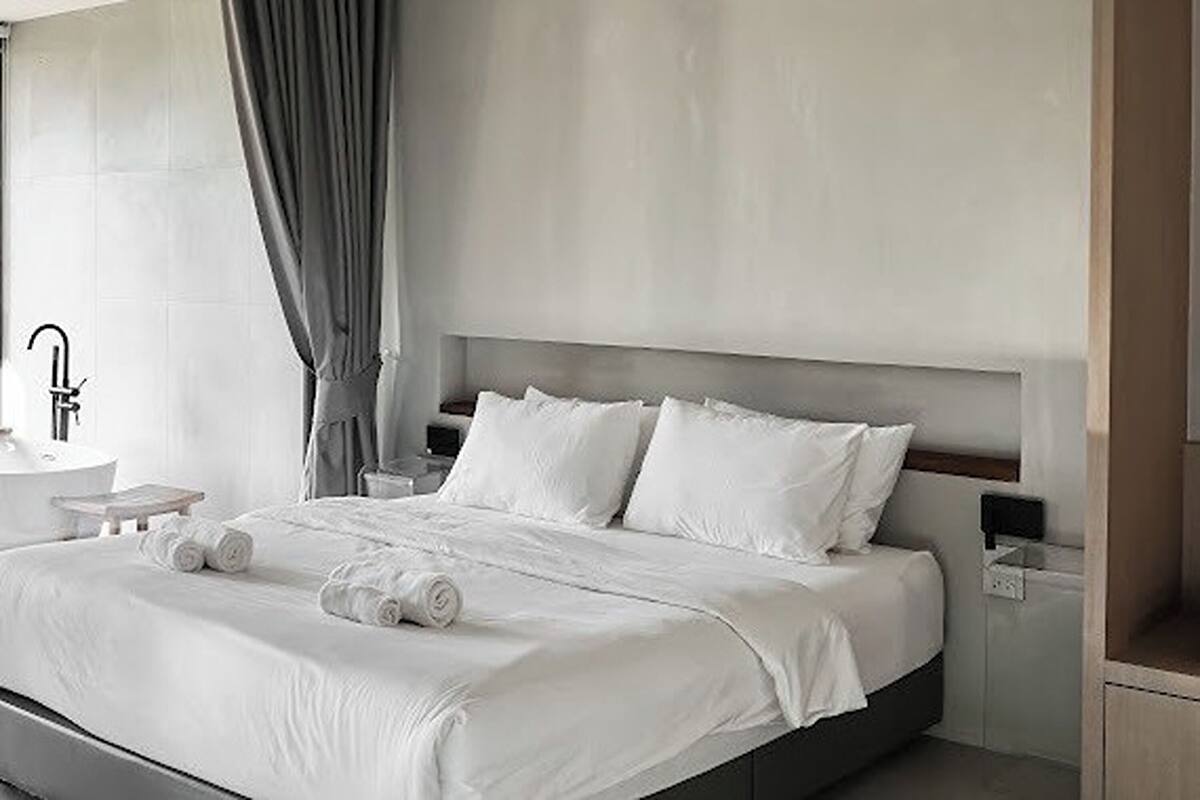 A modern hotel room with a large bed, a bedside table, a nightstand, and a window with curtains.