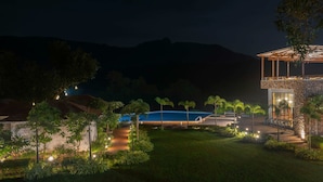 Una vista nocturna de un complejo turístico con piscina, edificio de piedra y senderos bien iluminados.