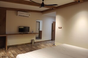 A bedroom with a bed, a TV on a wooden shelf, an air conditioning unit, and a door leading to another room. - Nirva The Cottage Resort, Kondeshwar Road Badlapur (Ambernath)