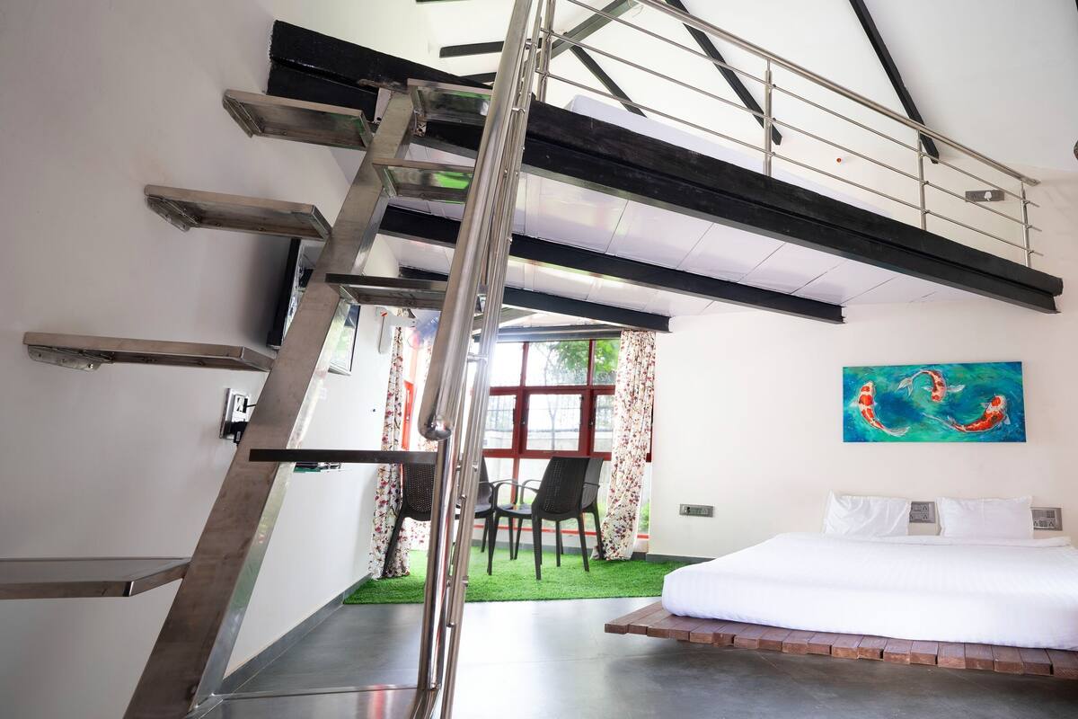 A bedroom with a bed, a painting, a staircase, and a view of the outdoors.