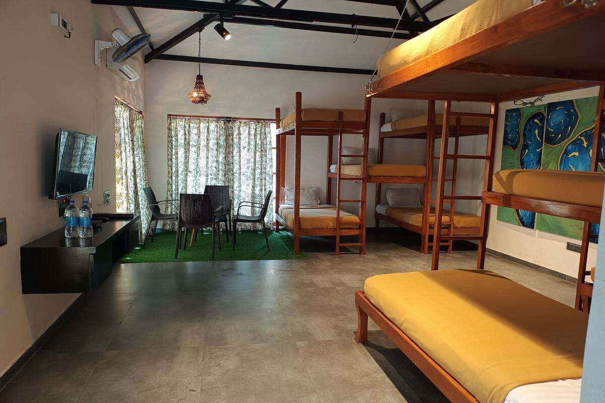 A room with bunk beds, a desk with a chair, a television, and a painting on the wall.