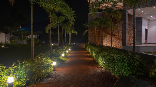 Un sendero bordeado de palmeras e iluminado con luces en el suelo, que lleva a un edificio con paredes de piedra y diseño moderno.