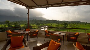 Terraza con mobiliario de mimbre y cojines anaranjados, con vistas a un paisaje verde que incluye un río y colinas distantes.