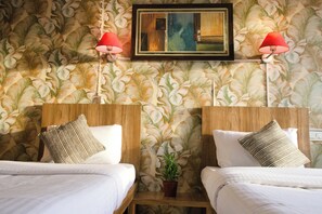 Une chambre d’hôtel avec deux lits, une tête de lit en bois, une plante en pot et deux lampes fixées au mur.
