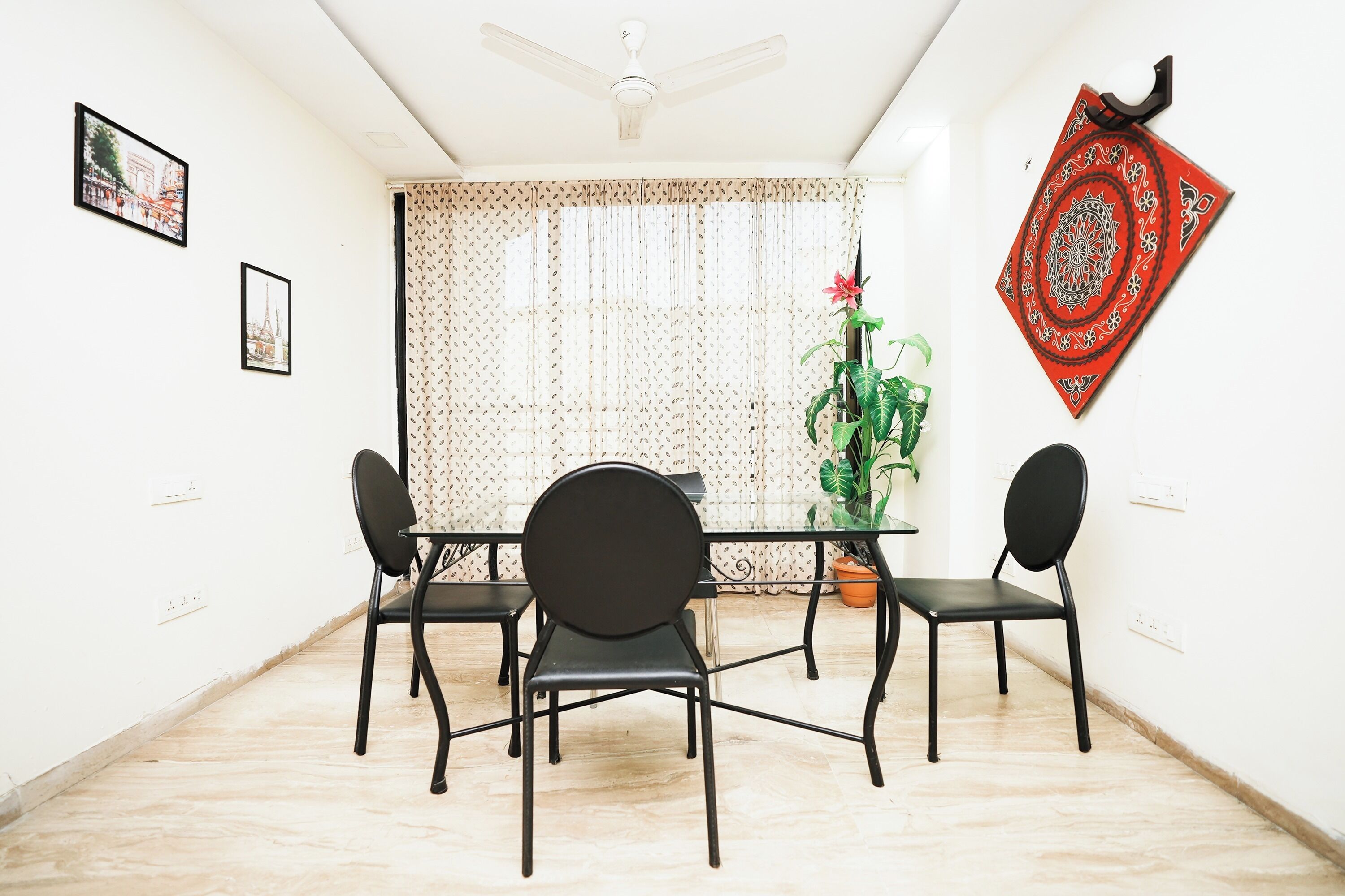 A dining area with a table and four chairs, a ceiling fan, a patterned curtain, and a red decorative item on the wall.