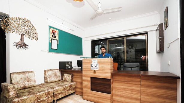 A reception area with a wooden desk, a green wall, and a sofa. - K.A.E Residency (Mumbai)