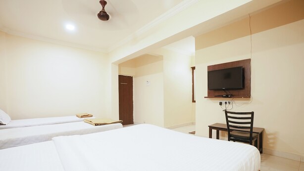 A hotel room with two beds, a TV mounted on the wall, and a desk with a chair. - Hotel Della Comfort near Ambreshwar Shiv Mandir, Ambernath (Ambernath)