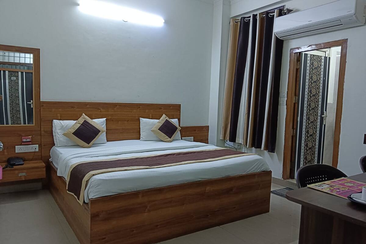 A bedroom with a wooden bed, two pillows, a bedside table with a phone, and a window with curtains.