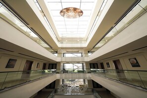 A multi-level atrium with a central water feature, glass railings, and a chandelier. - Blue Moon Boutique (Gurugram)