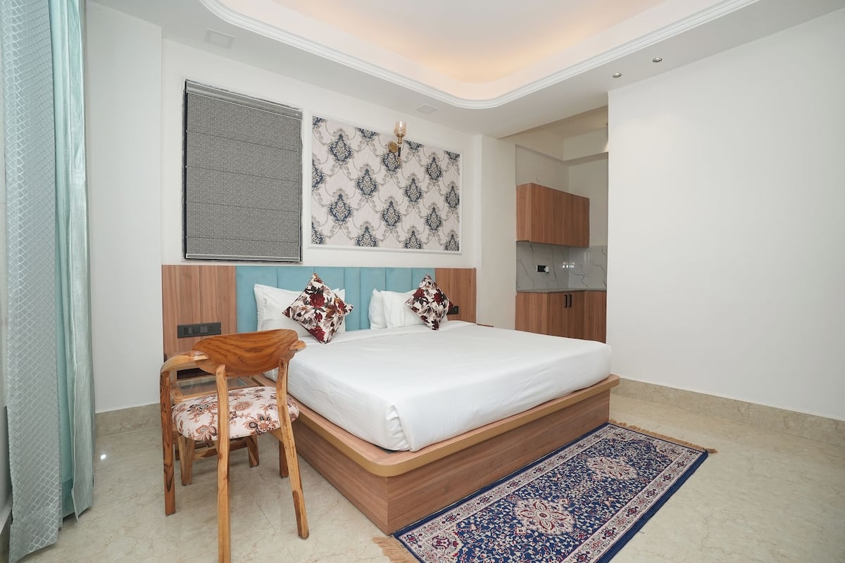 Un dormitorio con cama, una silla de madera, un tapete estampado y una ventana con persianas.