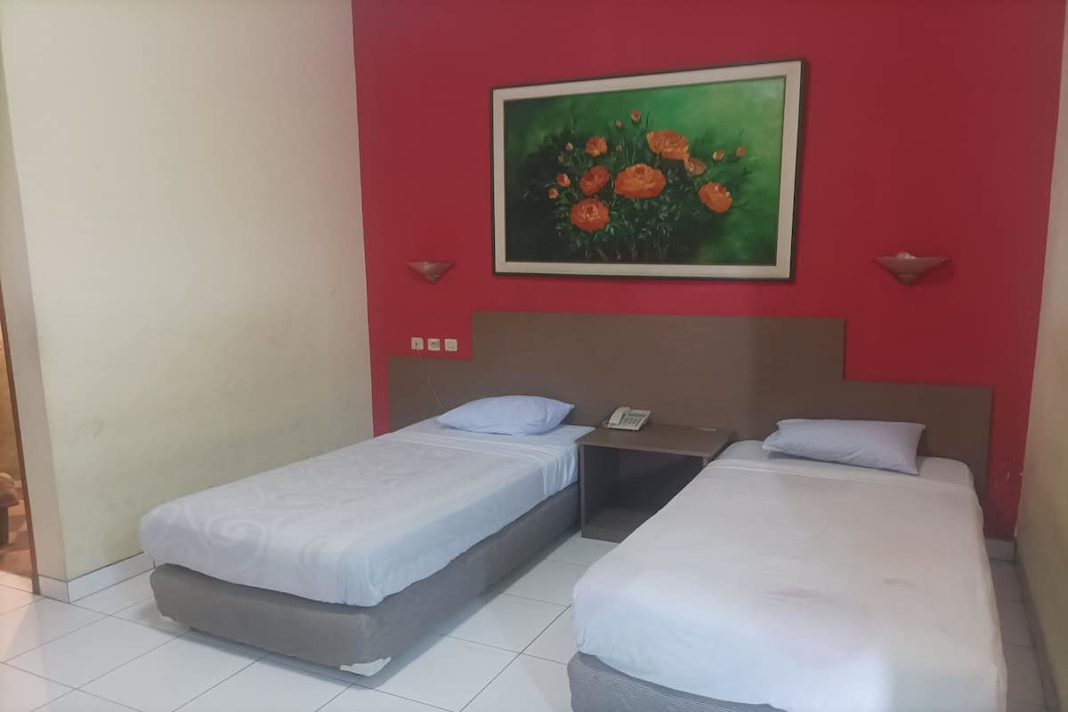 Une chambre d’hôtel avec deux lits simples, un mur d’accent rouge, un tableau représentant des fleurs et une petite table avec un téléphone.